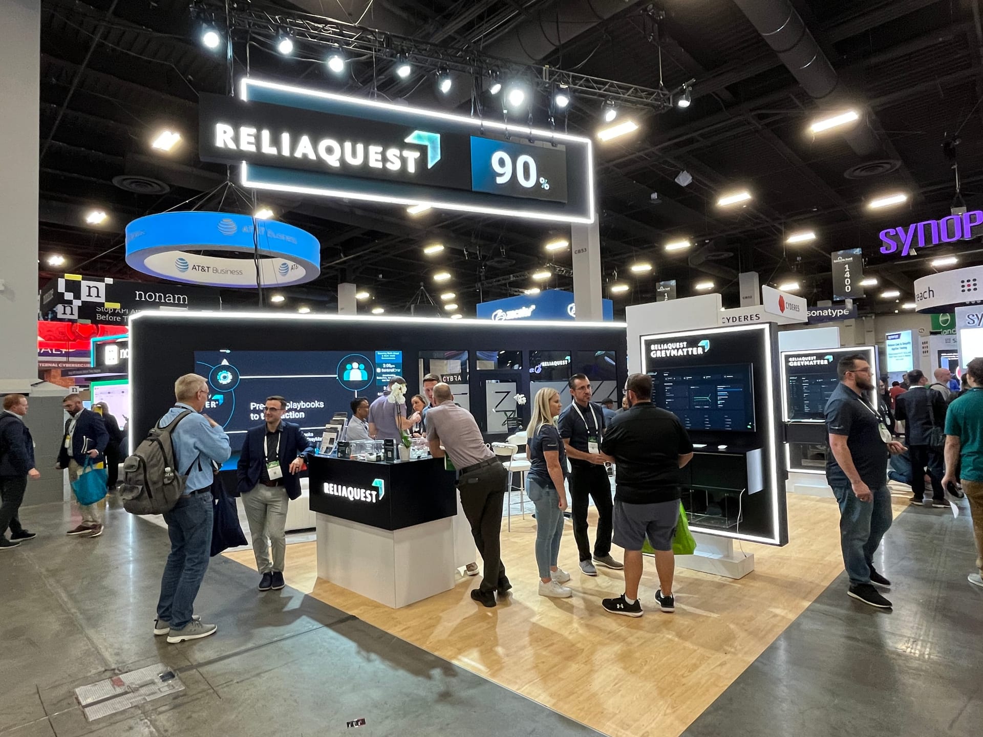 Busy ReliaQuest booth with suspended signage and demo stations full of attendees