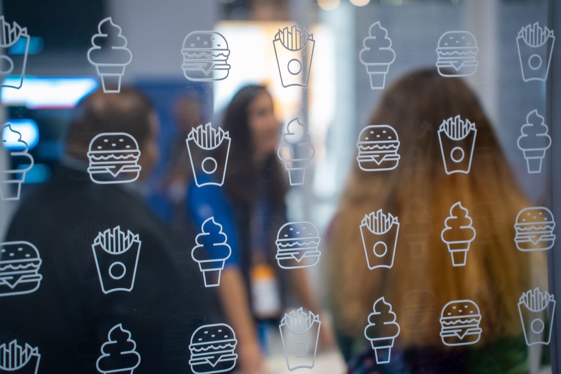 Close view of the IBM booth's glass wall printed with line icons of fries, burgers, drinks, and soft-serve, the show floor blurred beyond