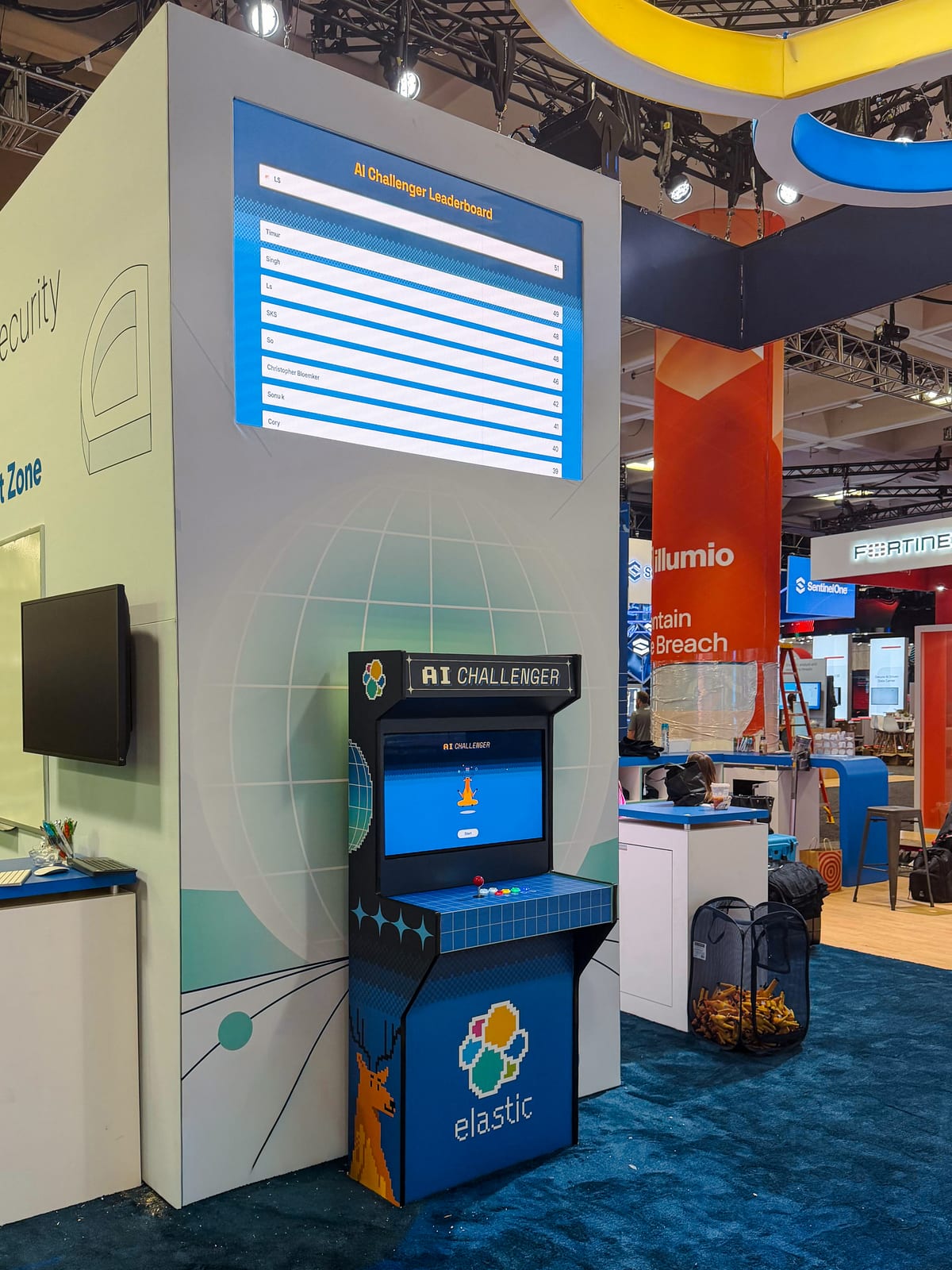 The Elastic AI Challenger arcade cabinet in booth 1111 at AWS re:Invent, beneath an LED leaderboard showing player scores