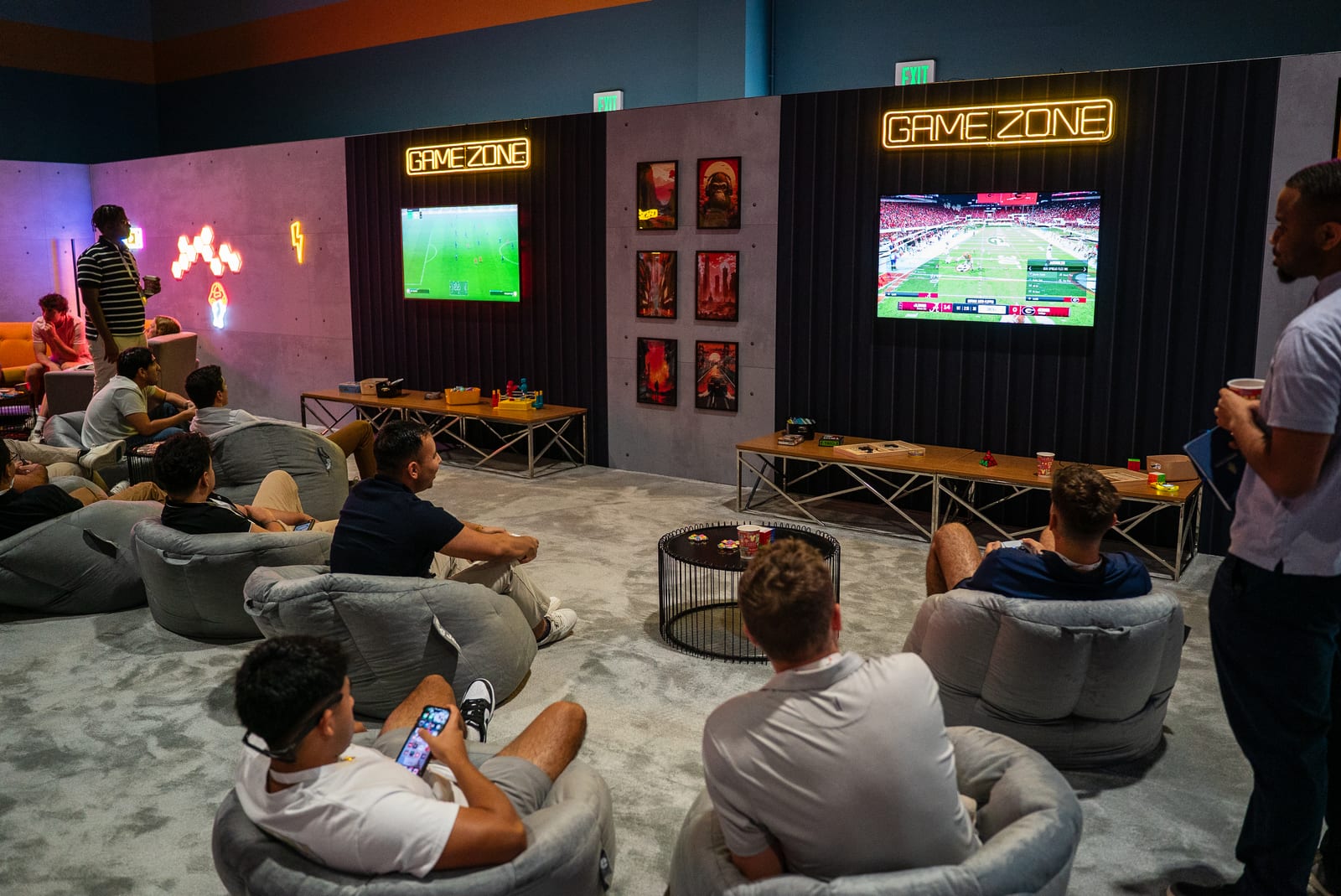 The Game Zone at PwC Impact 2024, neon Game Zone signs over wall-mounted screens running console games above a lounge of beanbag chairs
