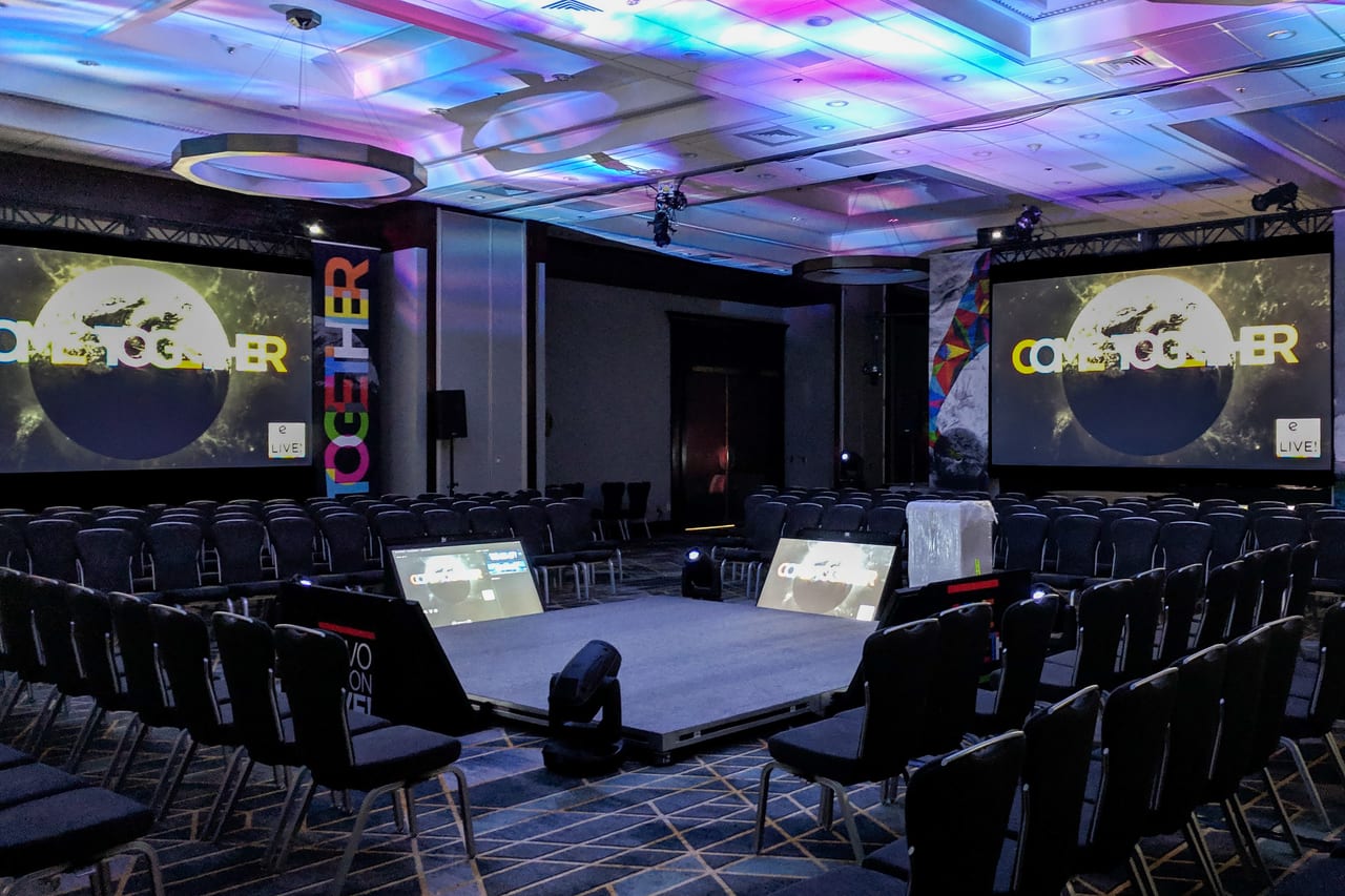 The Revolution Live general session lit before doors, Come Together across both fast-fold screens, color washing the ballroom ceiling and confidence monitors on the riser