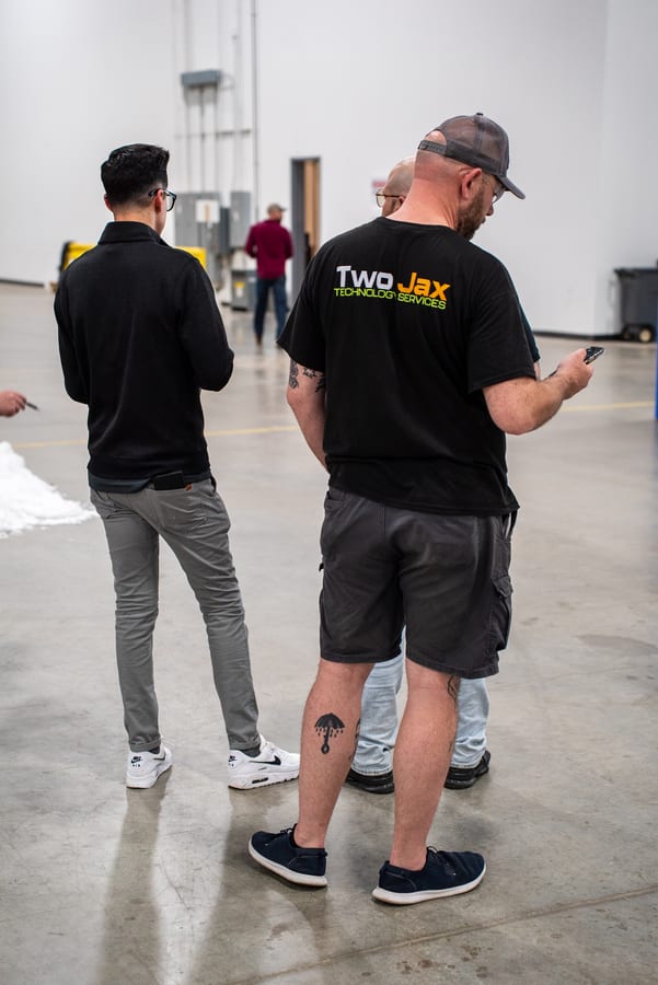 Two crew members in Two Jax shirts on the warehouse floor, checking something on a phone between tasks